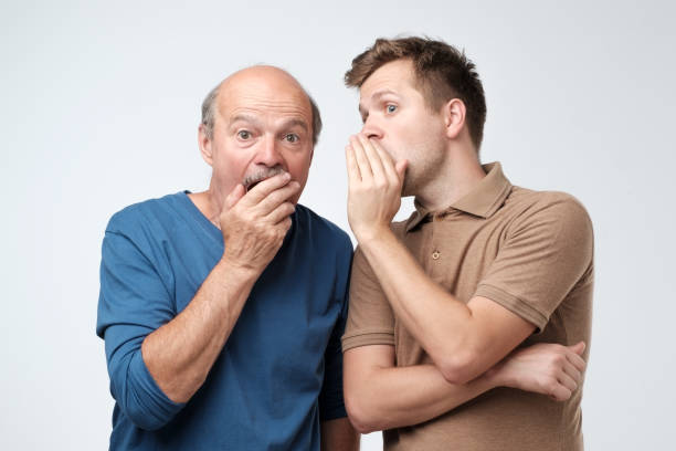 Young caucasian son telling secret to his senior father. Senior man in shock opening his mouth. stock photo