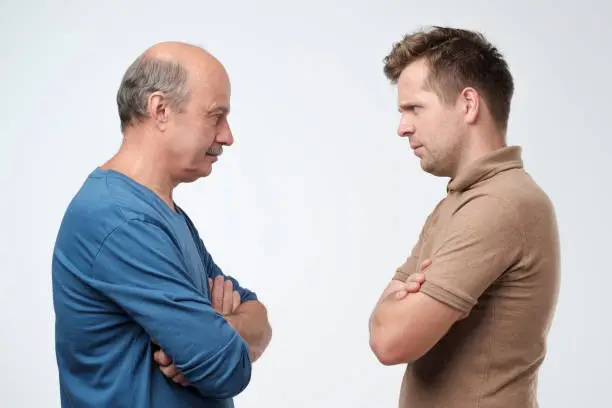 Mature father and son looking on each other face to face. They quarreled. To make claims and reproaches