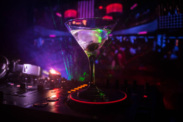 Glass with martini with olive inside on dj controller in night club. Dj Console with club drink at music party in nightclub with disco lights. Close up view stock photo