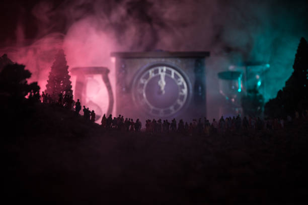 Silhouette of a large crowd of people in forest at night standing against a big arrow clock with toned light beams on foggy background. Time concept. Silhouette of a large crowd of people in forest at night standing against a big arrow clock with toned light beams on foggy background. Time concept. Hourglass measuring the passing time cologne germany stock pictures, royalty-free photos & images