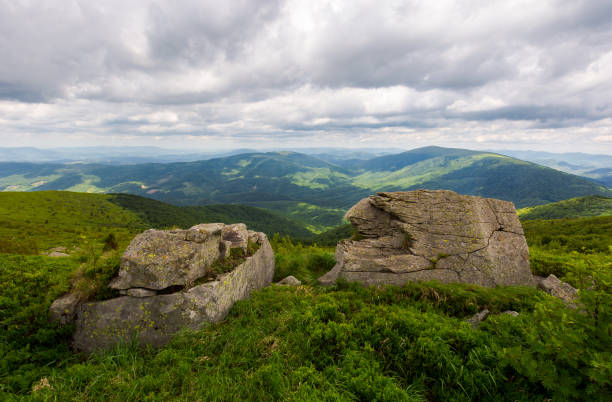 two boulders on the grassy hill. mountain range in the distance. overcast sky in summer
