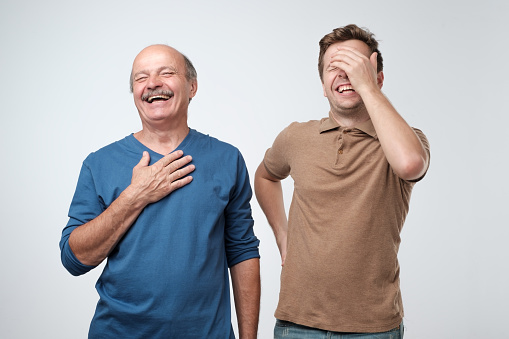 Two friends in casual colorful wear standing and laughing together. Mature son and father together chortling . Two men having fun.