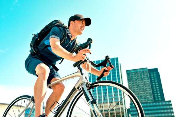 istock Man with backpack commutes to work on bicycle and rides past office buildings 1017631300