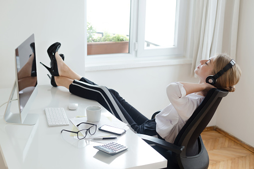 Young businesswomen with feet up on desk listening music