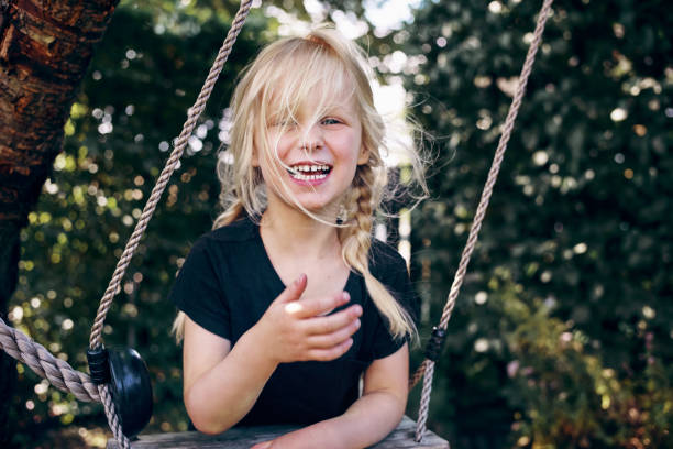 Laughing little blonde girl playing alone on a tree swing in her backyard on a sunny day