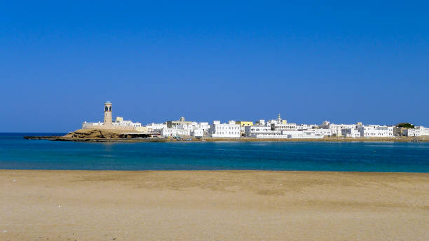 vista da cidade de sur, omã, com edifícios caiados de branco e farol, estendendo-se para as águas azuis - oman town arabia arabian peninsula - fotografias e filmes do acervo