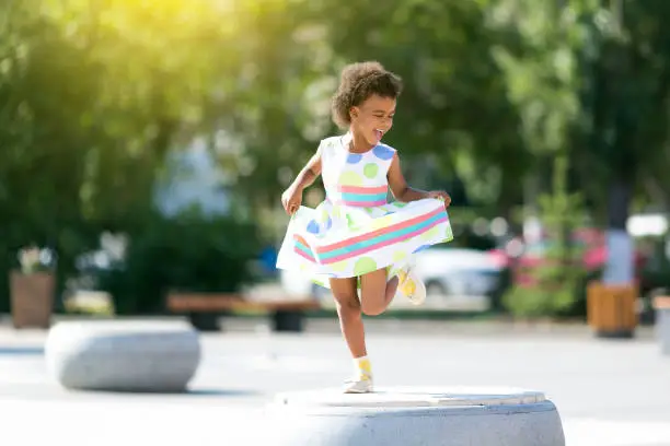 A child of an African-American woman dancing on a city street holding a dress in her hands.
