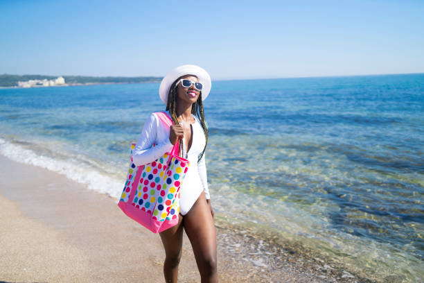 African woman enjoying summer vacations on beach, walking on sand.