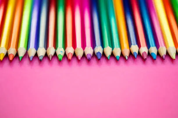 Photo of Color pencils in a row  on pink  background. Education, school  concept. Seamless colored pensils Close up.