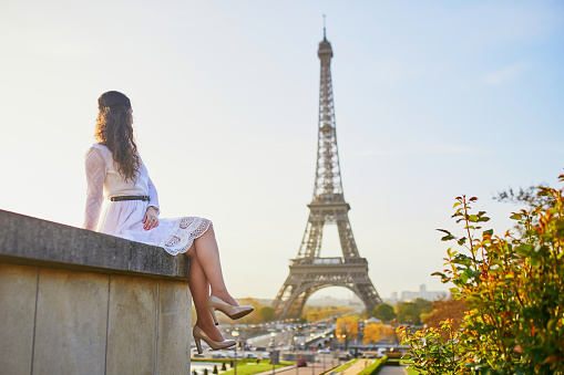 Happy young woman in white dress near the Eiffel tower in Paris, France
