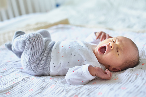 Adorable newborn baby girl sleeping and yawning in bed at home