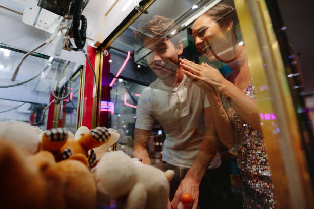 Man and woman having fun at a gaming arcade Happy couple having fun playing coin operated games at a gaming parlour. Man playing game at a gaming arcade while his girl friend cheers him. arcade photos stock pictures, royalty-free photos & images