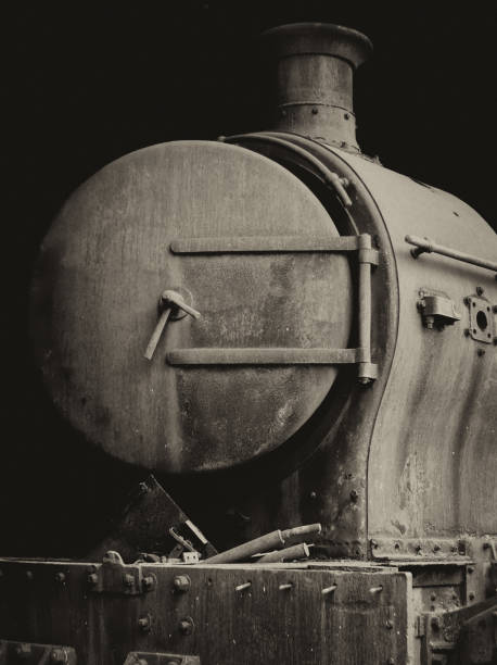 monochrome image of a nold rusty steam locomotive with door and chimney front view on black background monochrome image of an old rusty steam locomotive with firebox door and chimney front view on a black background firebox steam engine part stock pictures, royalty-free photos & images