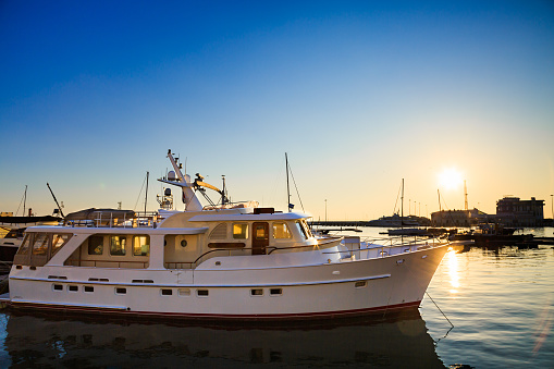 White yacht in commercial port, motor boats in Black sea at sunset.