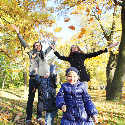 Happy family playing with autumn maple leaves in park at sunny day