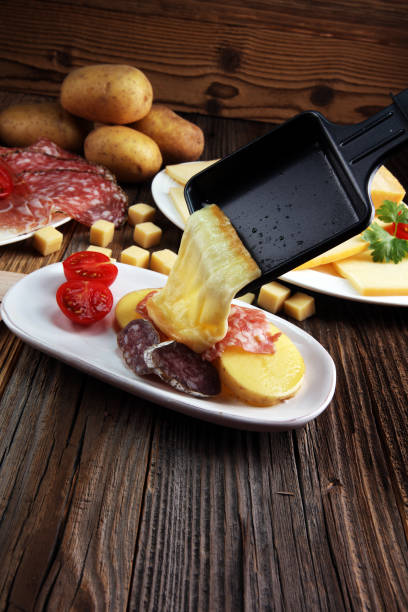 вкусный традиционный швейцарский плавленый сыр раклетт на нарезанный кубиками отварной или запеченный картофель. - raclette cheese стоковые фото и изображения