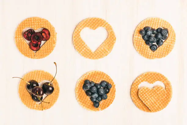 Traditional belgian waffles form of heart with fresh blueberry and sweet cherry on white wooden background. Flat lay, top view, copy space.
