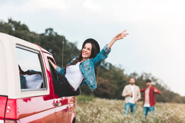 istock young woman outstretching from car window and raising hand while men standing blurred on background in flower field 1017887968