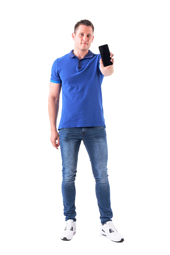 Cool young handsome adult casual man showing blank cell phone display at camera. Full body isolated on white background.