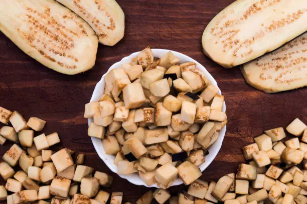 Photo of Eggplant crushed for use in the recipe in the form of cubes and wide flat slices on a wooden background.