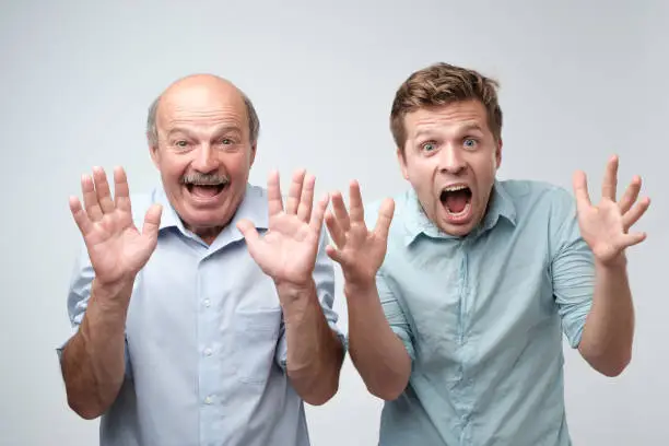 Curious shocked men, standing in casual shirts, isolated on pure background with wonderment. Father and son are shocked to know that their wifes are pregnant