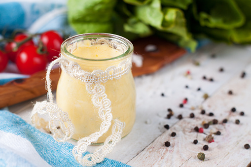 Homemade bearnaise or mayonnaise sauce in glass jar served with cherry tomatoes, greens, pepper