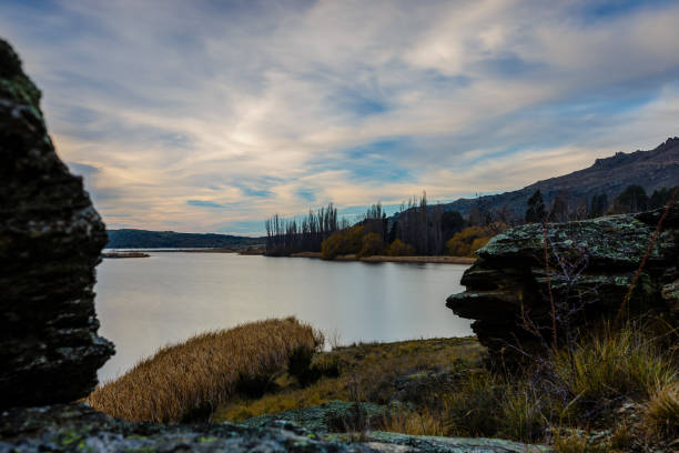 soyeux lisse central otago lac vu entre deux rochers avec un ciel nuageux - autumn sky nobody lake photos et images de collection