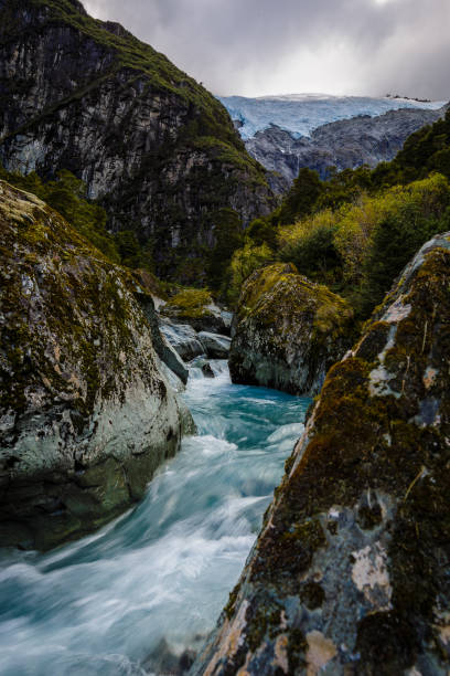 Alpine river flows between rocks with rob roy glacier in the background on a stormy day