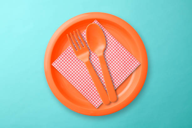 Overhead shot of orange plastic plate with Folk, Spoon, and Napkin on blue background.