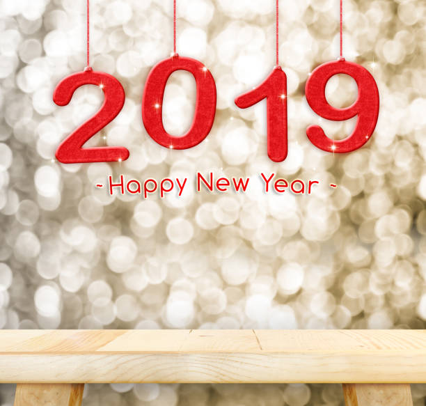 istock 2019 Happy new year hanging over plain wood table top with blur gold sparkling bokeh light,Holiday concept,leave space for adding your design. 1018011444