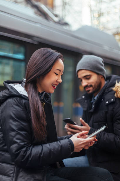 Young couple chatting, using smartphone on city street