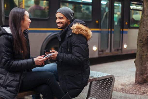 giovane coppia che chiacchiera, usa lo smartphone per city street - transportation bus mode of transport public transportation foto e immagini stock