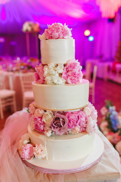 istock White wedding cake decorated with peony roses on pink restaurant background 1018062036