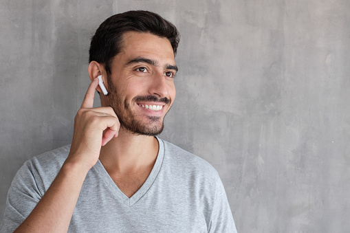 Young man wearing wireless earbuds and t shirt, listening to his favorite musical album online, touching one earphone to control application