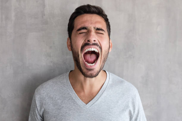 closeup portrait of screaming with closed eyes crazy young man, standing against gray textured wall - shouting imagens e fotografias de stock