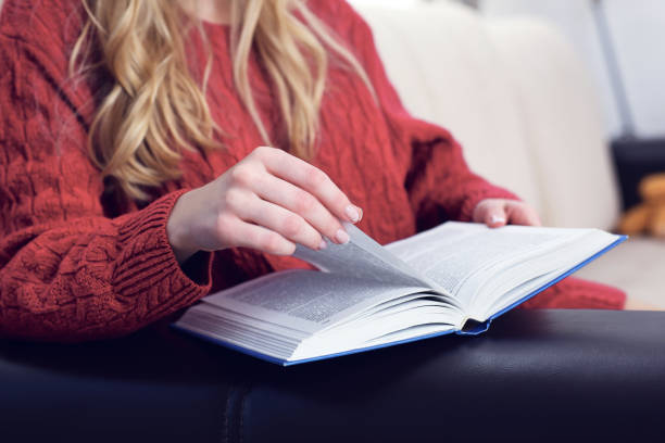 istock Middle section of young woman reading book at home interior background 1018088820