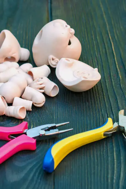 Photo of Parts of the BJD dolls and hand tools on a dark wooden surface. Concept of the craft of a master doll manufacturer. Vertical.