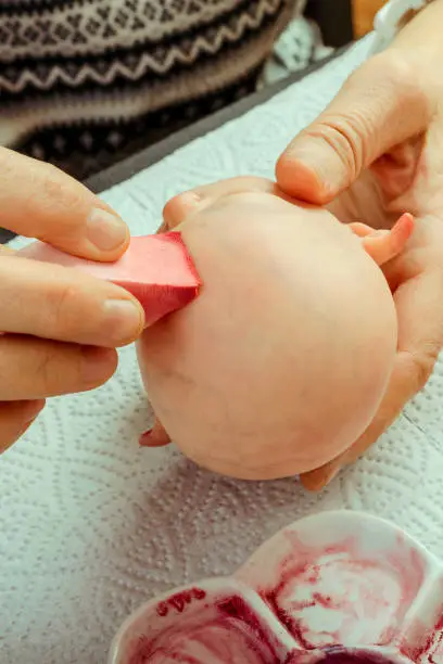 Photo of Female hands make dolls of BJD or reborn in the workplace. Processing the workpiece. The concept of the craft of the master manufacturer of dolls. Selective focus. Vertical.