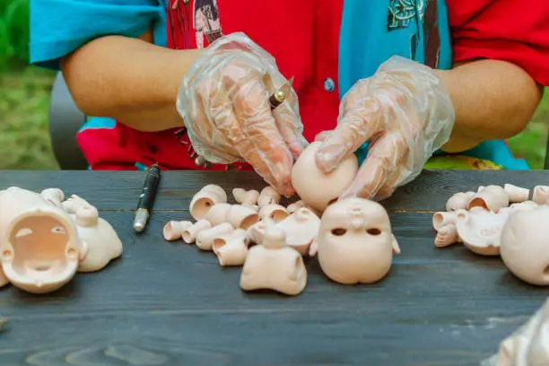 Photo of Female hands make dolls of BJD in the workplace. Processing the workpiece. The concept of the craft of the master manufacturer of dolls. Selective focus.