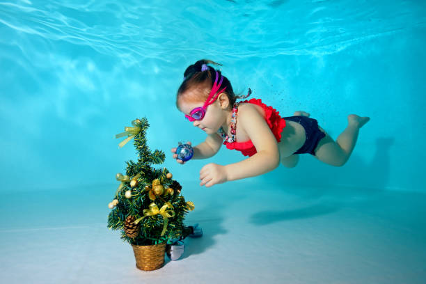 enfant sous l’eau dans la piscine décore le sapin de noël avec des jouets de noël. portrait. prise de vue sous l’eau. orientation horizontale - christmas child baby surprise photos et images de collection