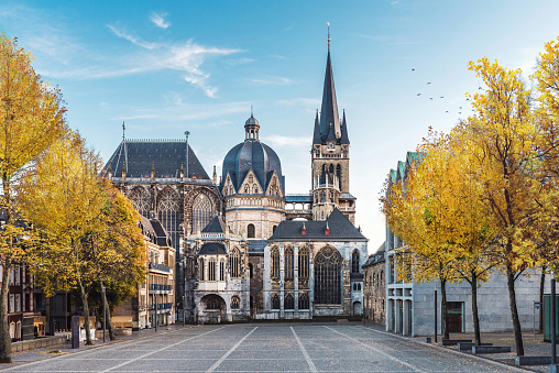 Huge gothic cathedral in Aachen Germany during autumn with yellow trees at Katschhof against blue sky in the background