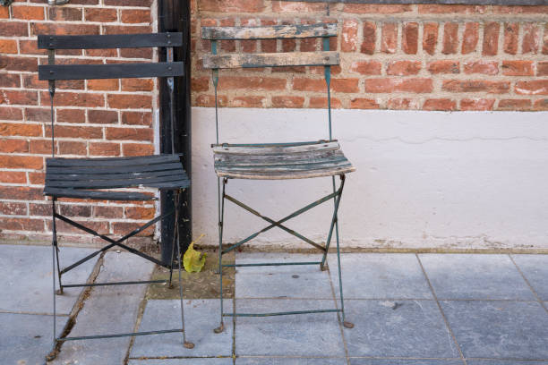 istock two empty broken wooden chairs on terrace, against brick wall 1018100060