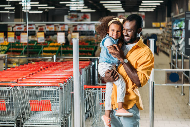 heureux homme afro-américain embrassant et maintenant la petite fille en épicerie - preschooler child offspring purity photos et images de collection