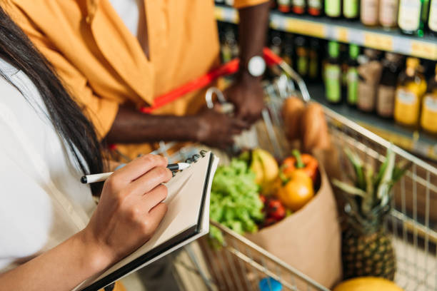 image recadrée de femme marquant la liste de courses tandis que son petit ami debout près avec chariot de supermarché - liste de courses photos et images de collection