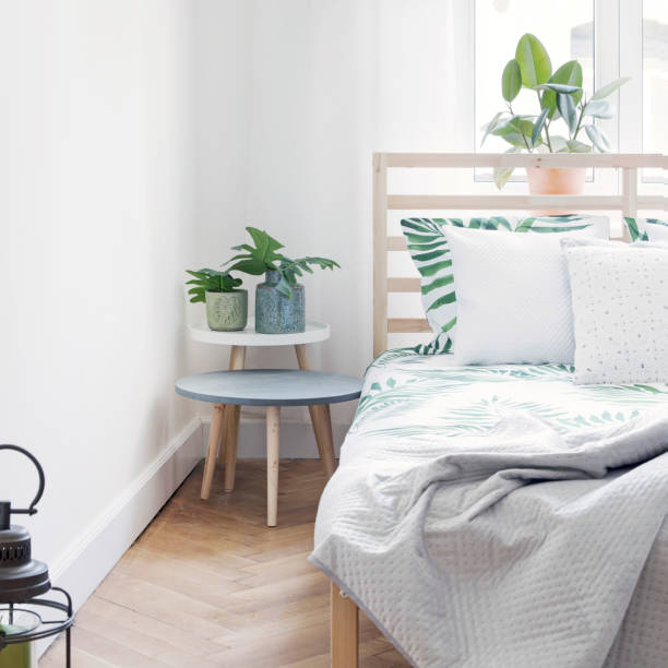 istock Modern scandinavian sunny bedroom with plants , floral pattern bedding and pilows. Space with white walls and brown wooden parquet. 1018117716