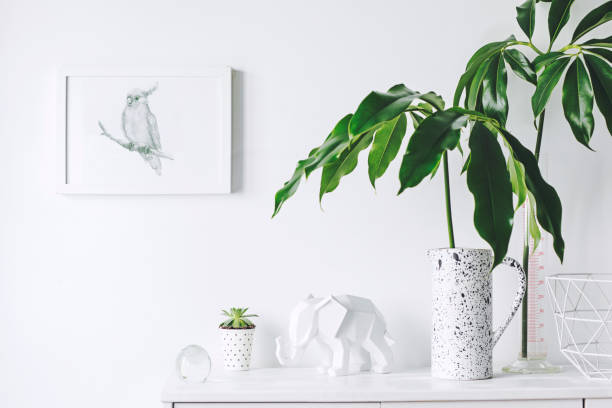 istock Stylish and modern white interior with mock up frame , elephant figures., tropical leaf and cacti White concept of cupboard shelf. 1018121400