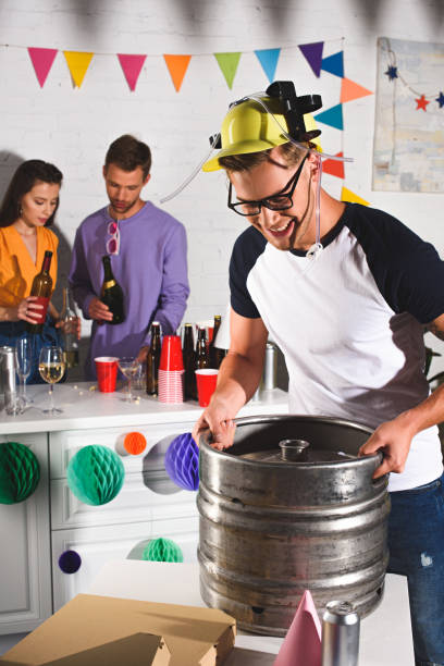 istock smiling young man holding beer barrel while friends drinking behind 1018135034