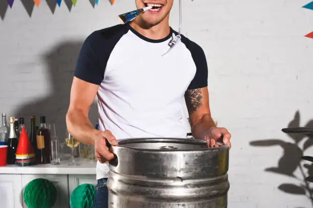 cropped shot of happy young man holding barrel of beer at home party