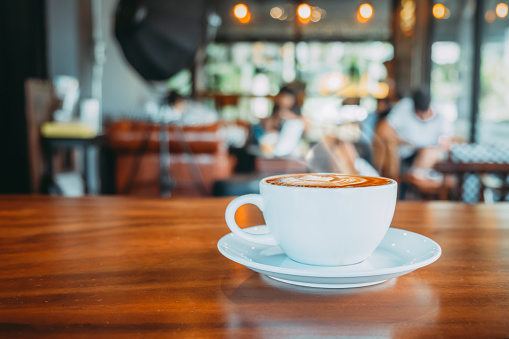 White cup of hot coffee on table in cafe with people. vintage and retro color effect - shallow depth of field