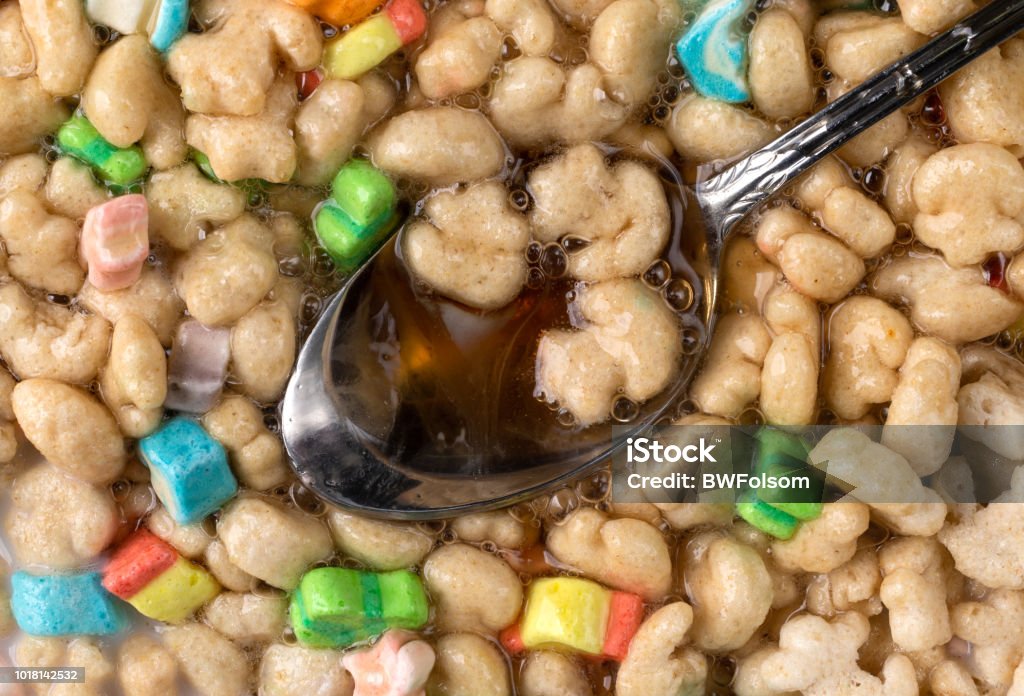 Crunchy breakfast cereal with milk and syrup Top close view of a spoon in generic crunchy breakfast cereal with fruit flavored bits plus milk and maple syrup. Blue Stock Photo